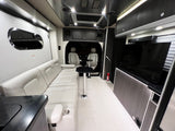 Interior of an upscale RV rental featuring a comfy sofa, dining tables, TV, & front cabin view for travel comfort.