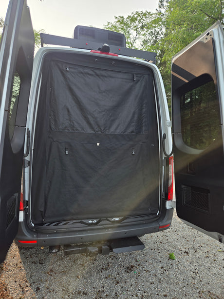 Rear of an RV rental camper van with doors open, revealing a black privacy screen. Features a roof AC unit and tow hitch.