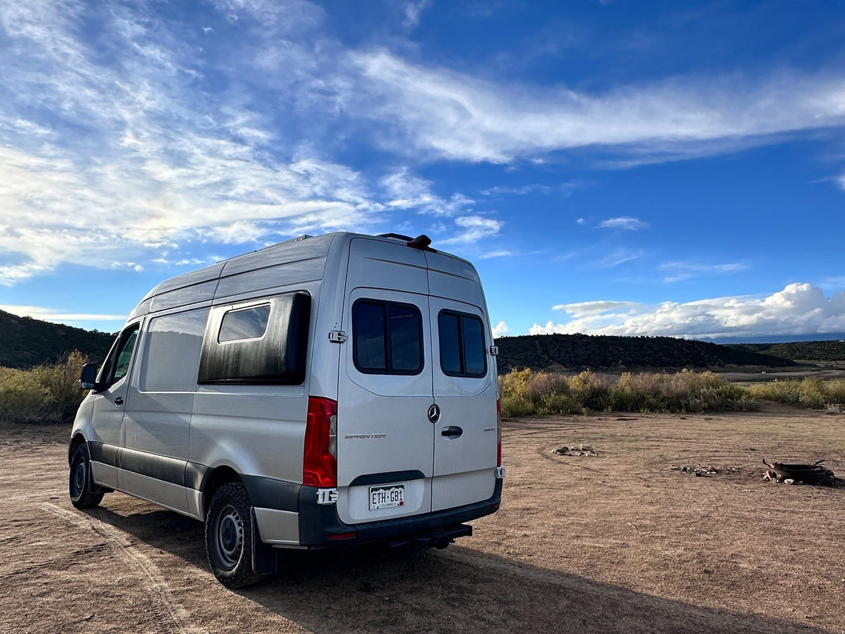  parked on a dirt road with mountains and clouds.|Explore the outdoors! This silver Mercedes Sprinter RV rental shows its custom campervan conversion interior. Van life ready.|Explore nature with an RV rental! A silver Mercedes Sprinter camper van is parked on a dirt road in a scenic — photo 3