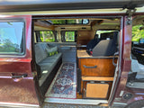 Step inside this RV rental! Cozy camper van interior with a seating area, kitchen, and comfy rug for your travels.