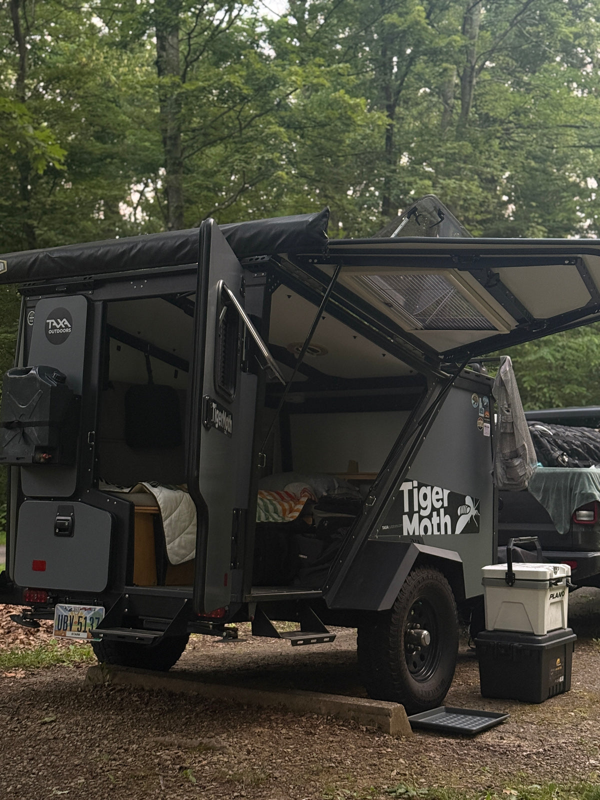 A Taxa Outdoors Tiger Moth off-road trailer, possibly an RV rental, is set up at a campsite with its doors open, ready for adventure. — photo 10