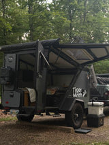 A Taxa Outdoors Tiger Moth off-road trailer, possibly an RV rental, is set up at a campsite with its doors open, ready for adventure.