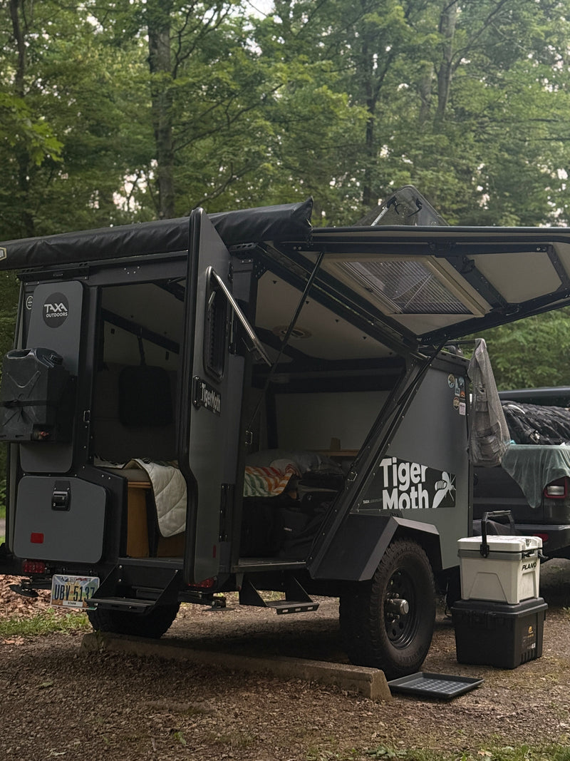 A Taxa Outdoors Tiger Moth off-road trailer, possibly an RV rental, is set up at a campsite with its doors open, ready for adventure. — photo 10