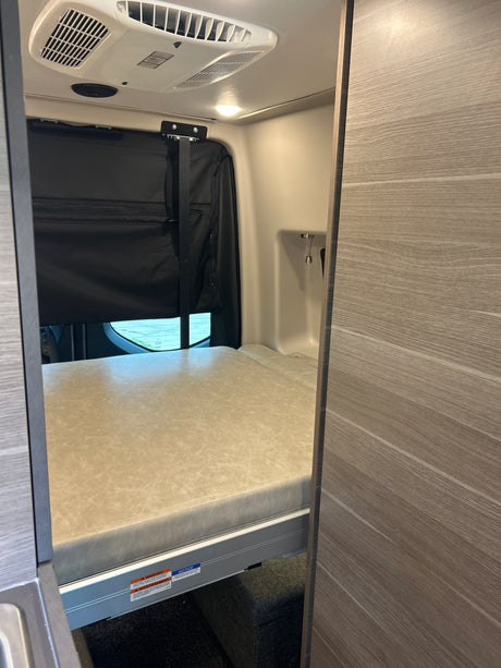 RV rental van interior features a comfy bed, ceiling AC, and window shades, ideal for road trips and mobile living.