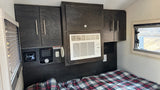 Cozy RV rental interior with bed, dark cabinetry, AC, heater, and control panel for comfort.