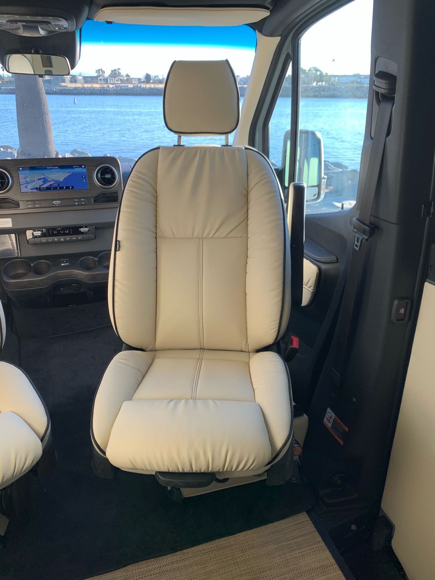 Luxurious RV rental interior: cream leather passenger seat, dashboard with nav screen, and scenic ocean view.