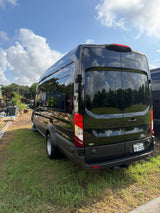 Rear of a black Ford Transit camper van, ideal for RV rental, parked on grass. Reflective surface shows sky & trees. Texas plate XXL-0132.