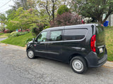 Black Ram ProMaster City van parked on street with flowering trees. Ideal for cargo, not an RV rental.