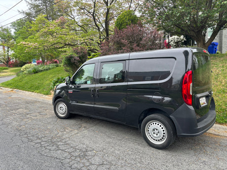 Black Ram ProMaster City van parked on street with flowering trees. Ideal for cargo, not an RV rental.