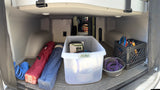 Inside an **rv rental's** rear **storage**, featuring organized **camping gear**: blue hose, bagged chairs, Hefty bin, dog bowl, and crate.