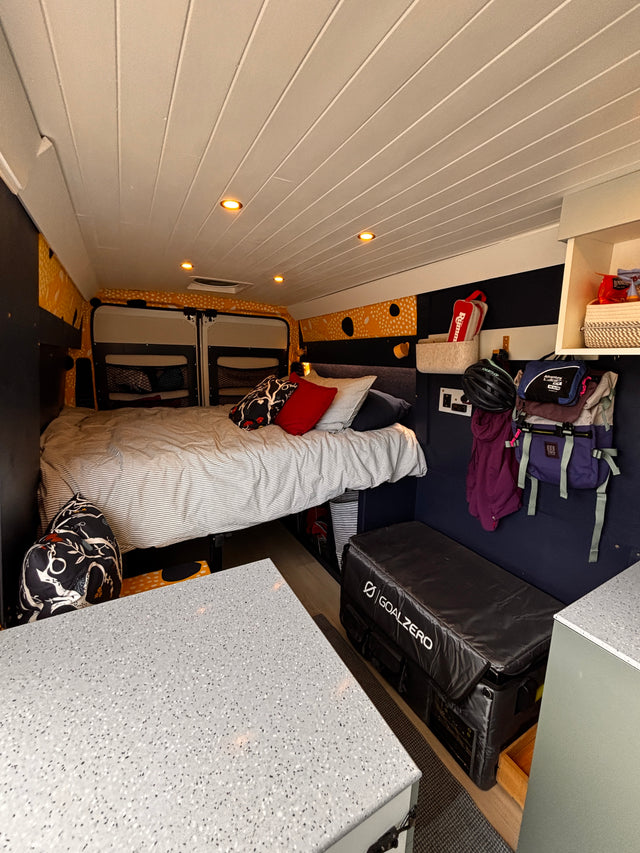 Cozy RV rental interior: A comfortable bed, ample storage including hanging gear, white slatted ceiling lights, and modern counter space.