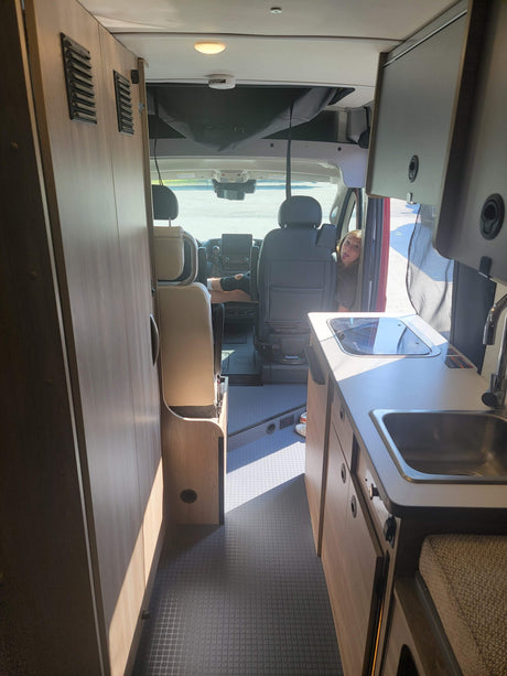 Inside a modern rv rental: kitchen, storage, and two people in the front seats, one playfully sticking out their tongue.