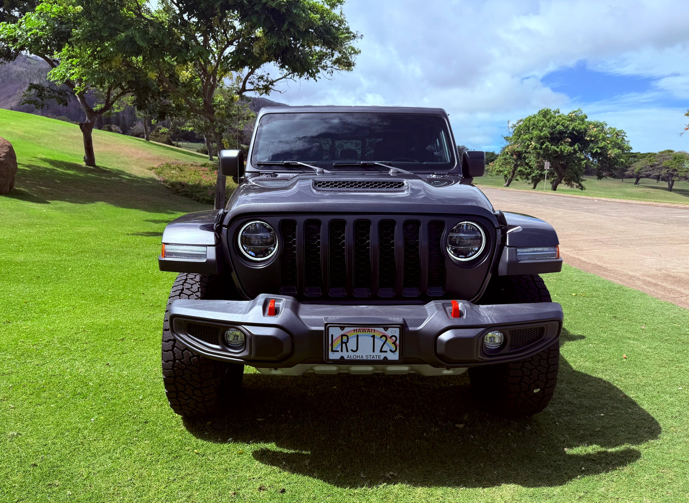 A dark gray Jeep on a Hawaii lawn, ready for an RV rental journey. Green grass, trees, and hills under a cloudy sky.