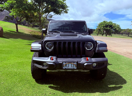 A dark gray Jeep on a Hawaii lawn, ready for an RV rental journey. Green grass, trees, and hills under a cloudy sky.