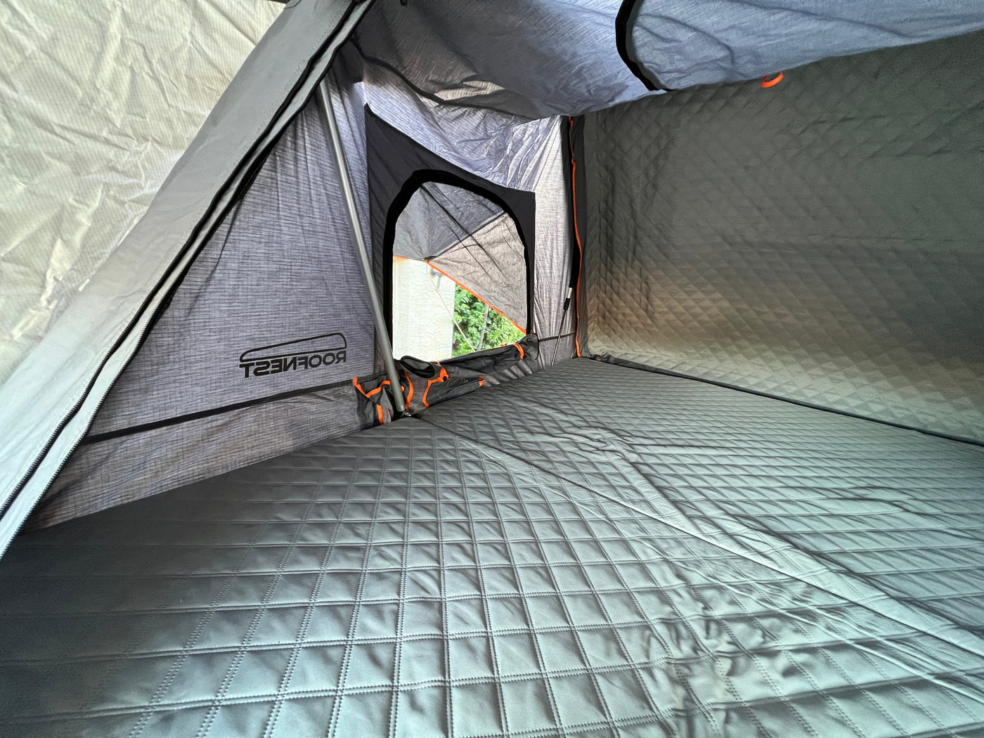 Inside a Roofnest roof-top tent: comfortable quilted mattress, storage, and an outside view. Ideal for your RV rental trip. — photo 7