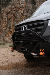 Rugged Mercedes-Benz Sprinter van with off-road features, wet from rain, parked on dirt near rocky cliffs. Ideal for rv rental.