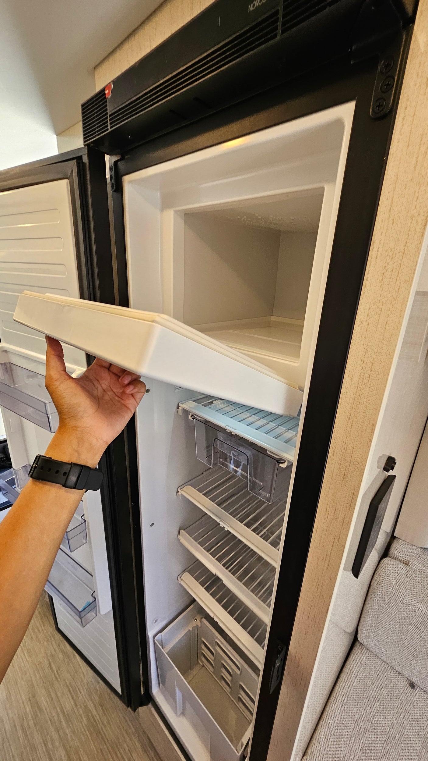 A hand holds a shelf inside an open RV rental refrigerator with a top freezer compartment, ready for your next adventure.