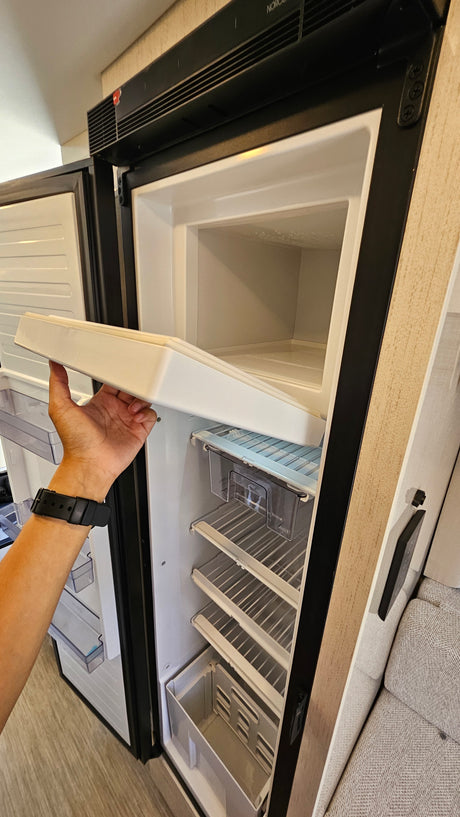 A hand holds a shelf inside an open RV rental refrigerator with a top freezer compartment, ready for your next adventure.