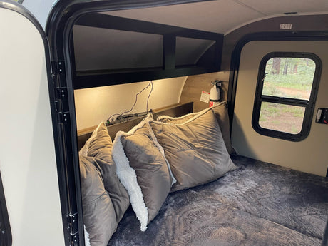 Cozy RV rental interior featuring a comfortable bed, overhead shelves, a fire extinguisher, and an exit door with a view.