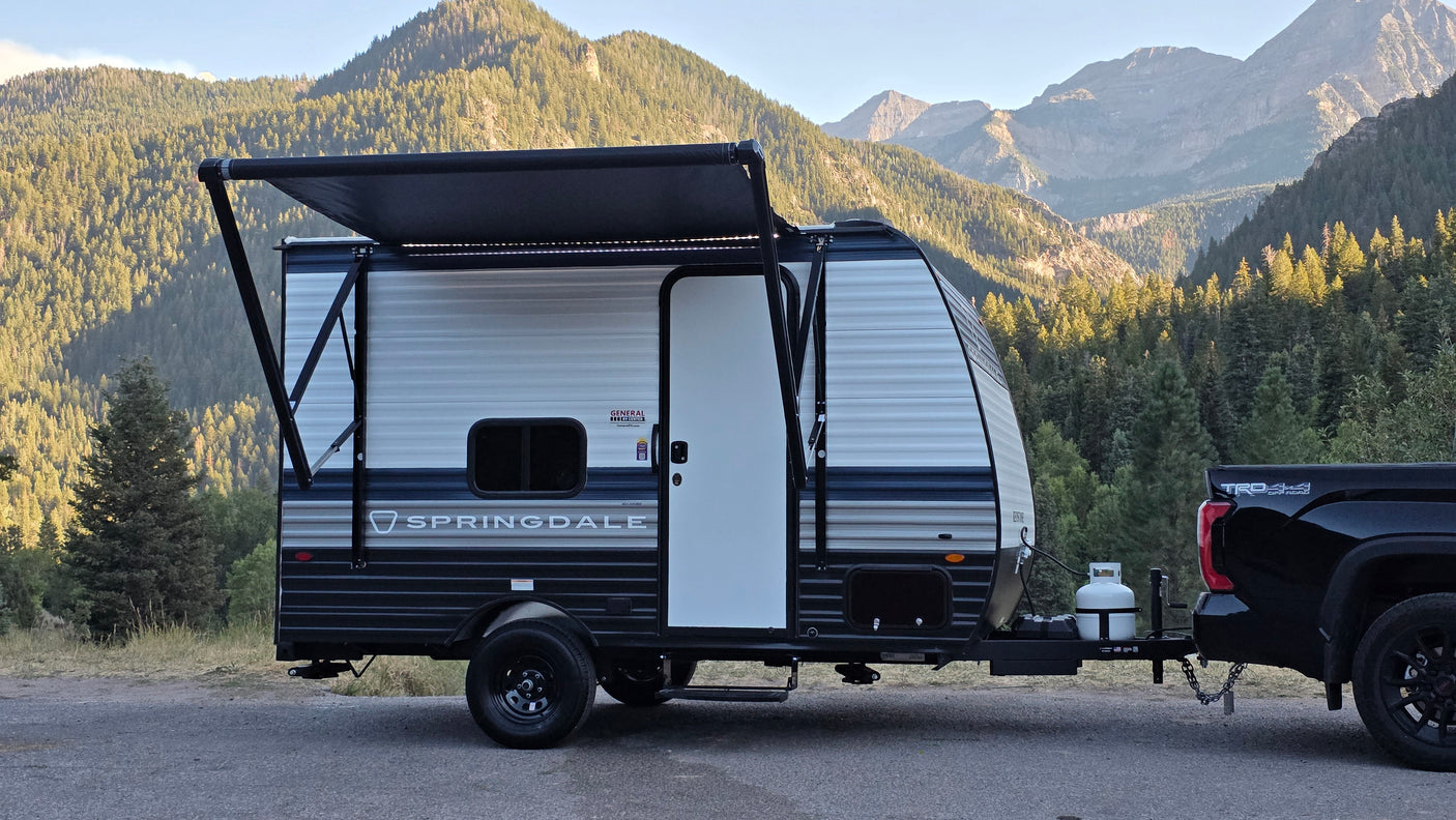 RV rental camping: A Springdale travel trailer hitched to a truck, parked in a scenic mountain setting with its awning extended.