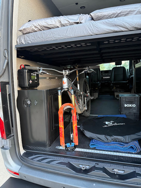 RV rental's clever design: a mountain bike secured under the elevated bed, with organized gear storage for adventures.