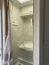 Compact RV rental bathroom with light-tiled walls, a corner toilet, and a grey-striped shower curtain.