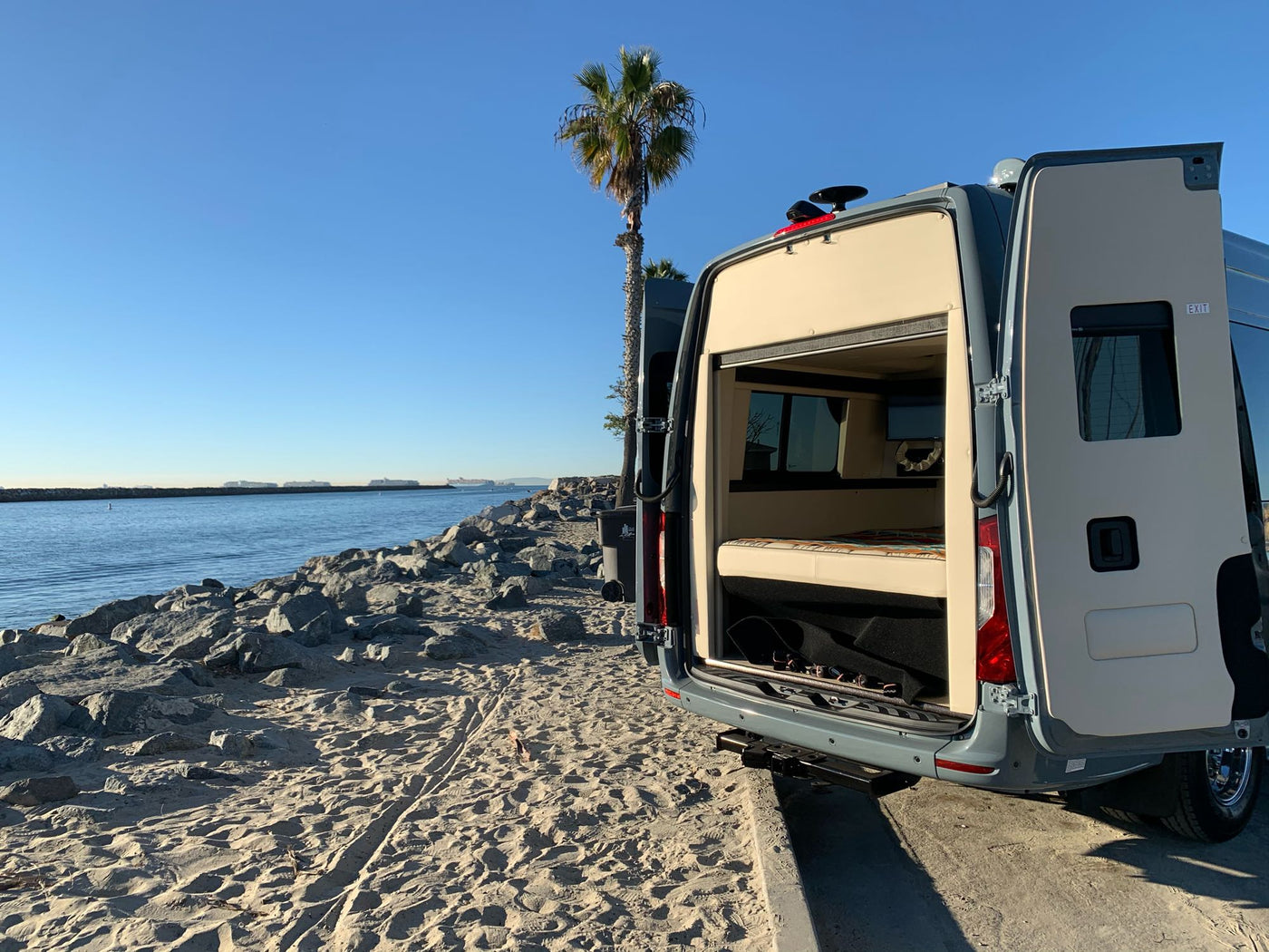  flanked by towering red rock cliffs under a cloudy sky.|Grey Sprinter RV rental with awning extended — photo 3