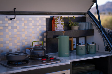 Compact RV rental kitchen with stove, coffee maker, and Stanley mugs, ideal for convenient outdoor cooking.