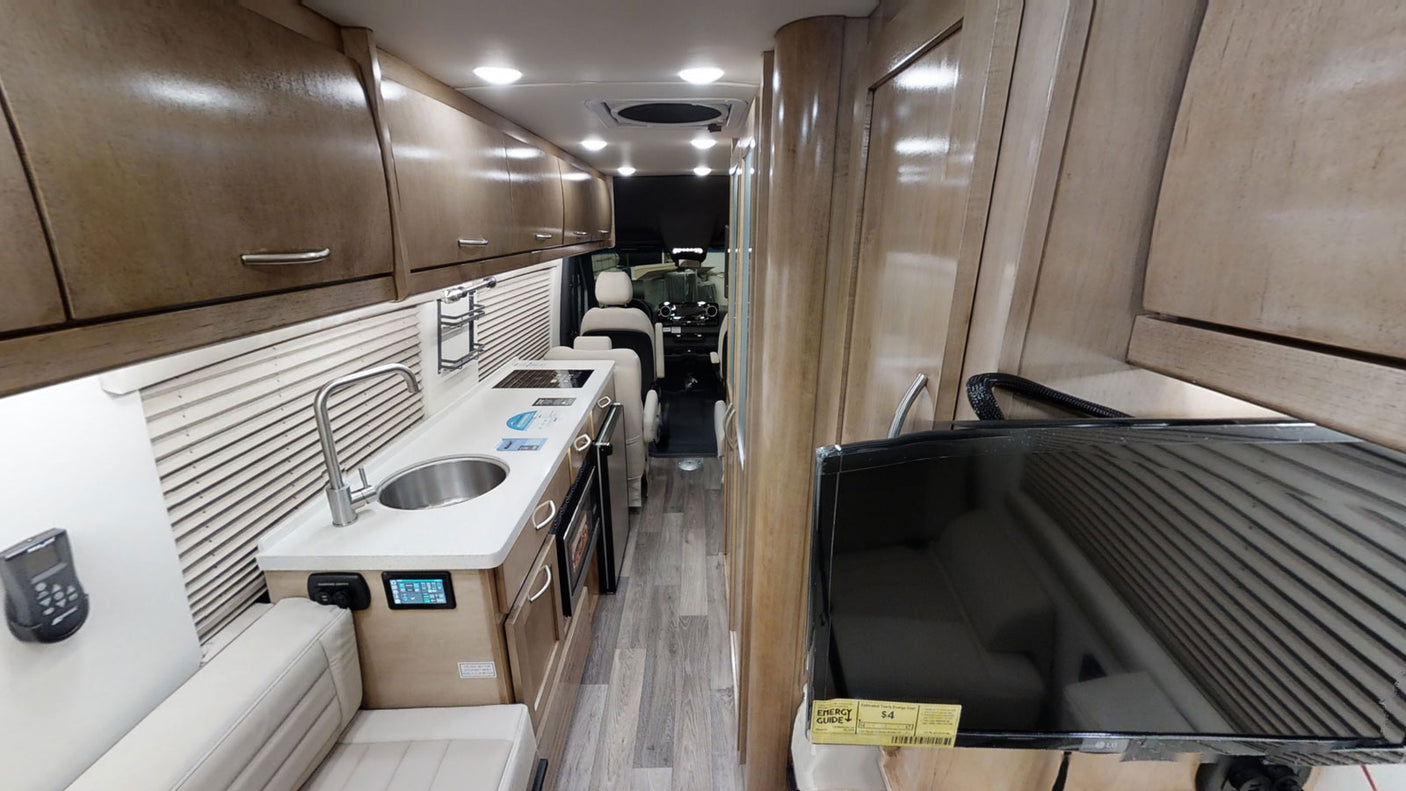 Interior of a modern rv rental, showing a compact kitchen with sink, lounge seating, and a view down the aisle to the driver's cabin.