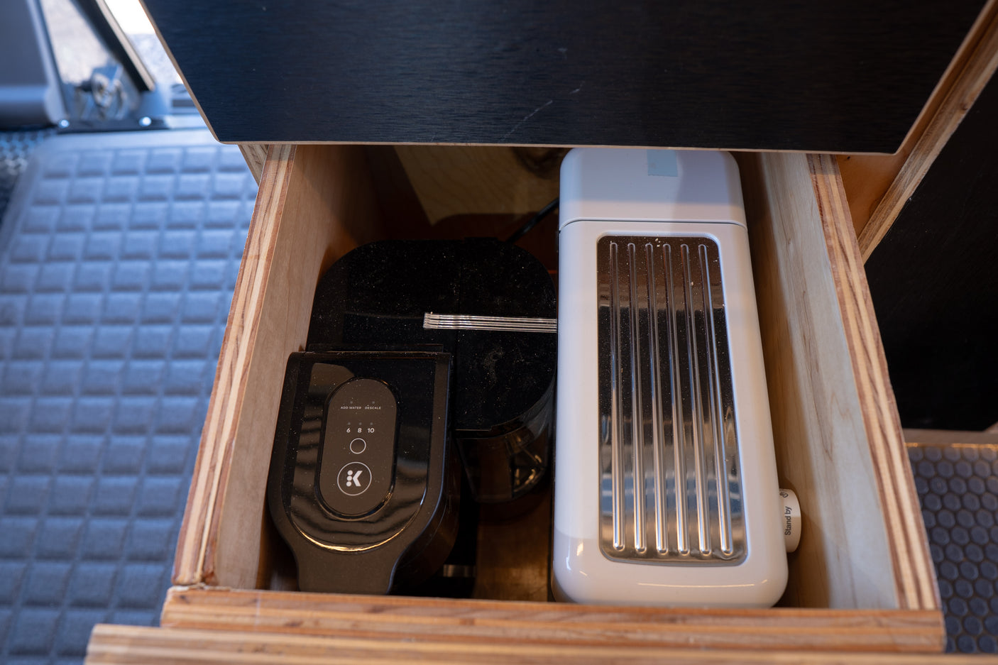 Keurig coffee maker and toaster stored in an RV rental's compact wooden kitchen drawer.