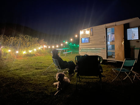 Night camping by an RV rental. String lights illuminate a person, dog, and vintage camper.