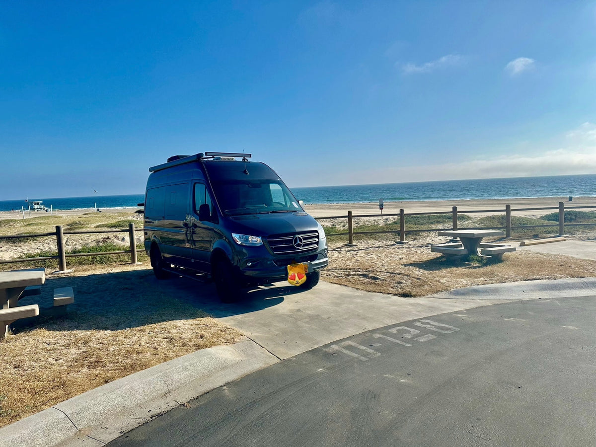Coastal camping with an RV rental: A dark camper van parked on a concrete pad with beach access