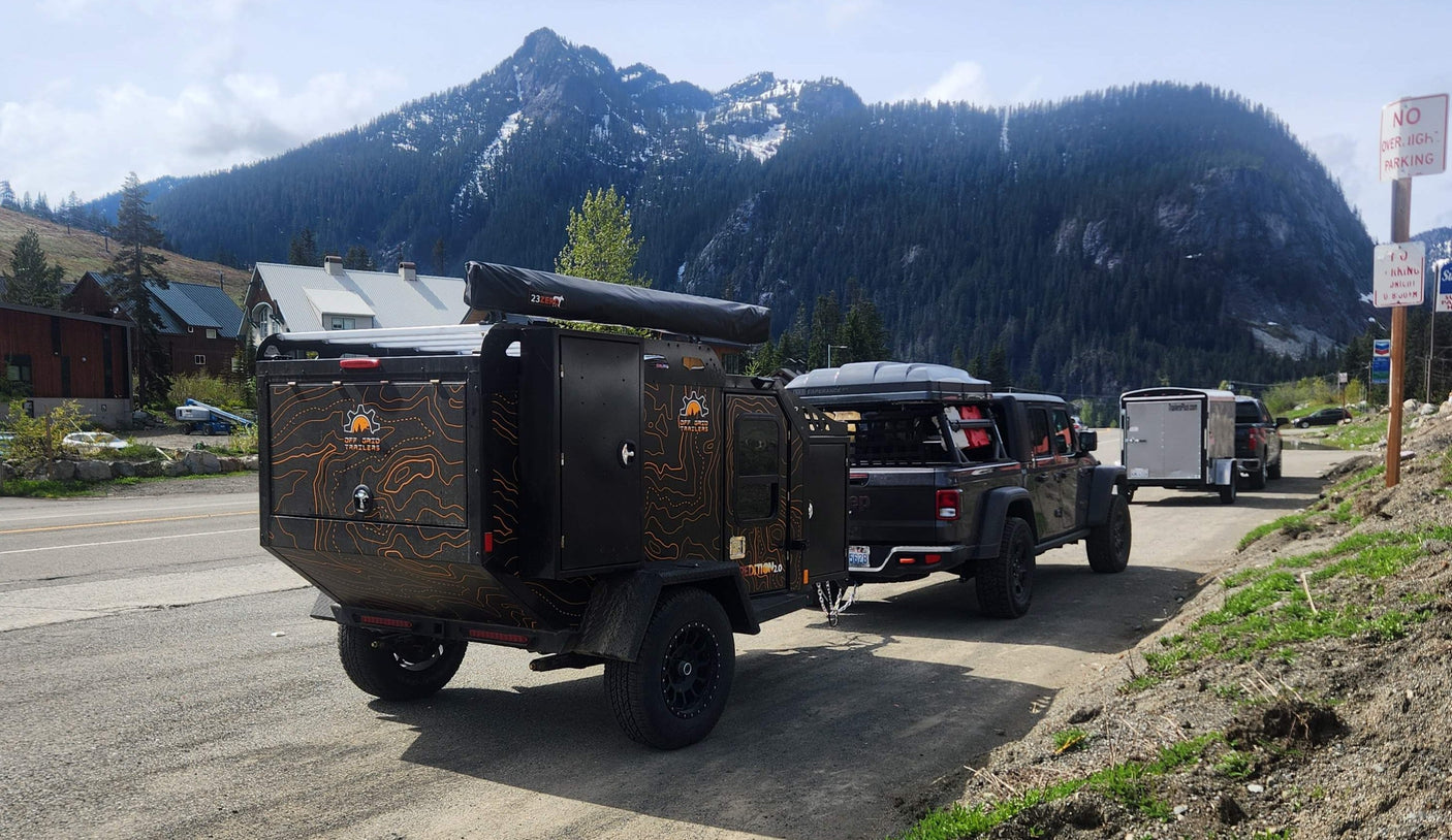 Ready for an rv rental journey: a rugged Off Grid overland trailer towed by a Jeep Gladiator, set against a stunning mountain backdrop.