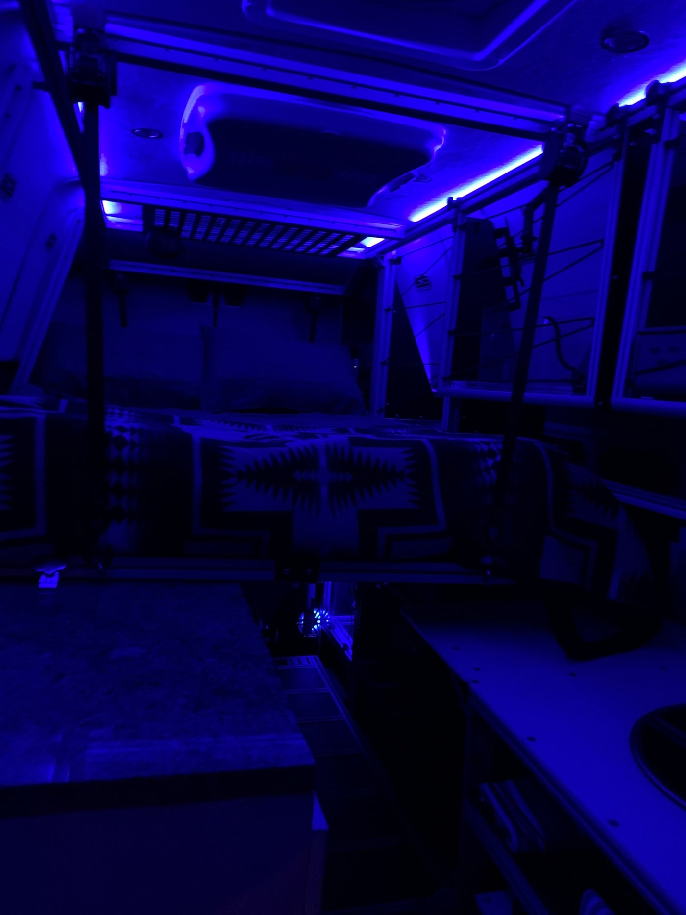 Immersive blue light fills this modern RV rental interior, showcasing a cozy bed and efficient storage. — photo 14
