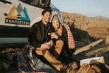 Joyful couple on their WanderVans rv rental, enjoying hot drinks by their van in a scenic outdoor setting.