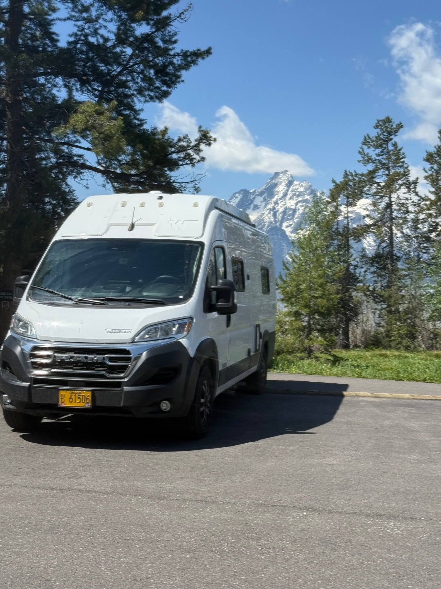 White Winnebago camper van rv rental parked against a backdrop of majestic, snow-capped mountains & pine trees.