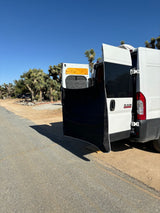 An RV rental van's open rear doors with a privacy screen set up, amidst Joshua trees on a sunny day.