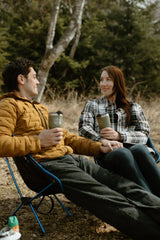 Enjoy nature with an rv rental! A couple holds hands, relaxing in camping chairs with coffee mugs in the peaceful outdoors.
