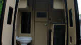 Inside an RV rental, a compact interior features a white toilet on the left and a kitchenette with a sink on the right.