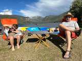 Relaxing lakeside with an RV rental! Family enjoys camping chairs, a paddleboard, and mountain views.