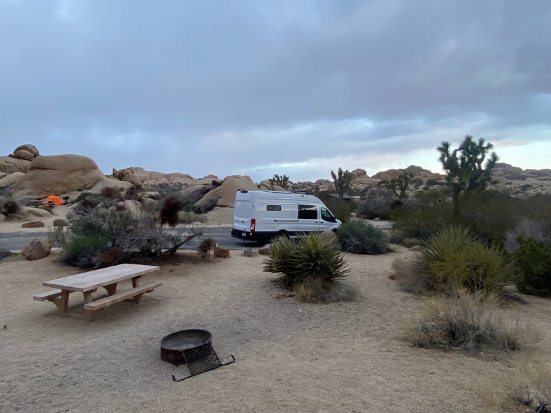  ideal for travel.|This white RV rental camper van is parked amidst Joshua trees and boulders in a sunny desert landscape — photo 8