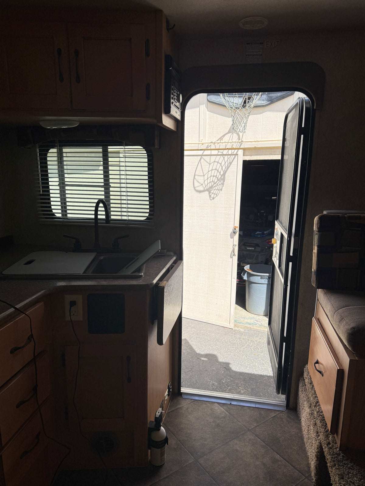 RV rental interior: kitchenette, seating, and open door revealing an outdoor basketball hoop's shadow on a building. — photo 13