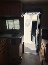 RV rental interior: kitchenette, seating, and open door revealing an outdoor basketball hoop's shadow on a building.