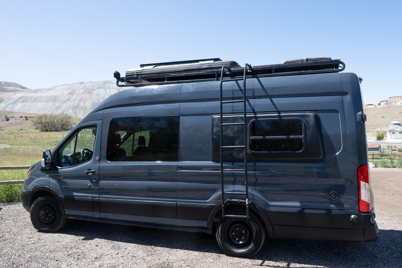 Side view of a dark gray customized camper van, ideal for rv rental adventures, with a roof rack and a ladder.