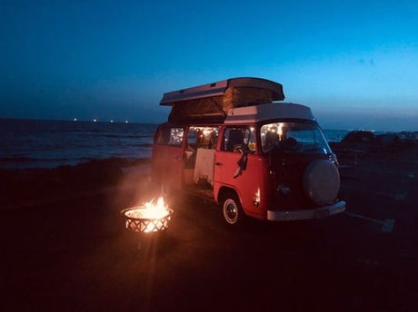 Vintage VW camper van (RV rental) parked on a dark beach at night, illuminated by a warm campfire. Perfect for coastal adventures.