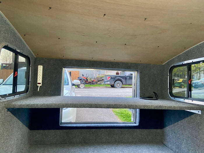 Inside an RV rental: a cozy space with carpeted walls, wooden ceiling, power strip, and scenic views from multiple windows.