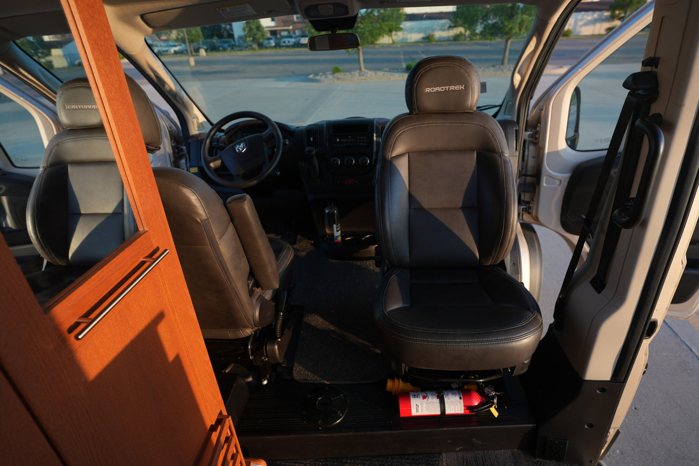 Roadtrek RV rental front cabin with dark leather seats, steering wheel, and dashboard. A fire extinguisher is visible by the passenger seat.