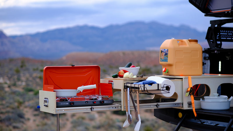 An RV rental's organized outdoor kitchen setup: stove, fresh vegetables, water jug, and cooking tools ready for adventure. — photo 7