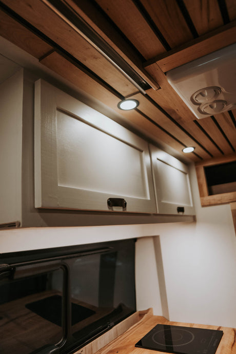 Modern RV rental kitchen featuring wood ceilings, integrated lights, light cabinets, an oven, and induction cooktop.