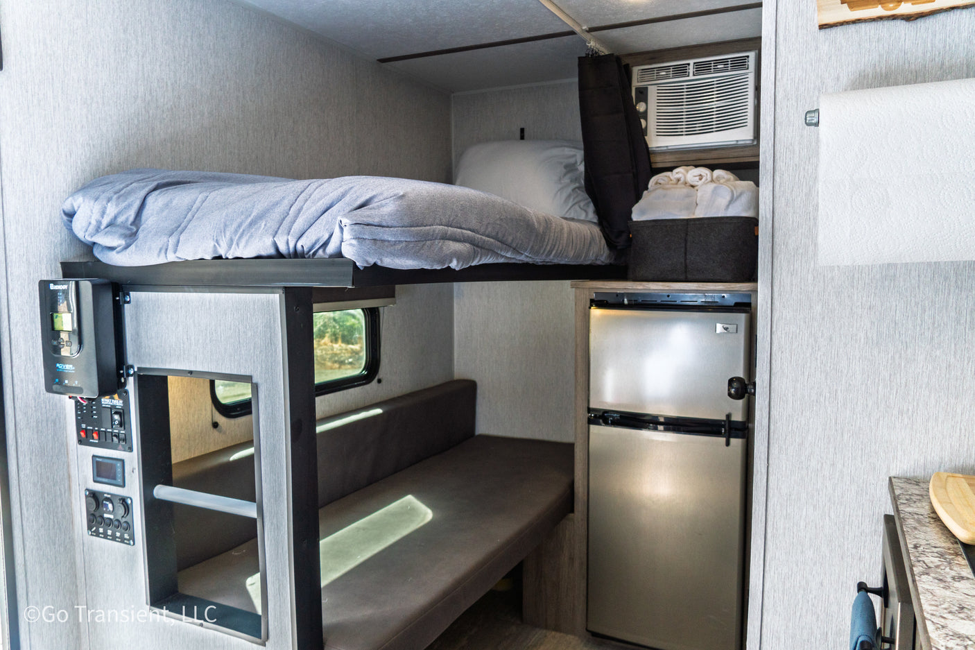 This RV rental interior offers a compact bunk bed, refrigerator, AC unit, and flexible dinette space.